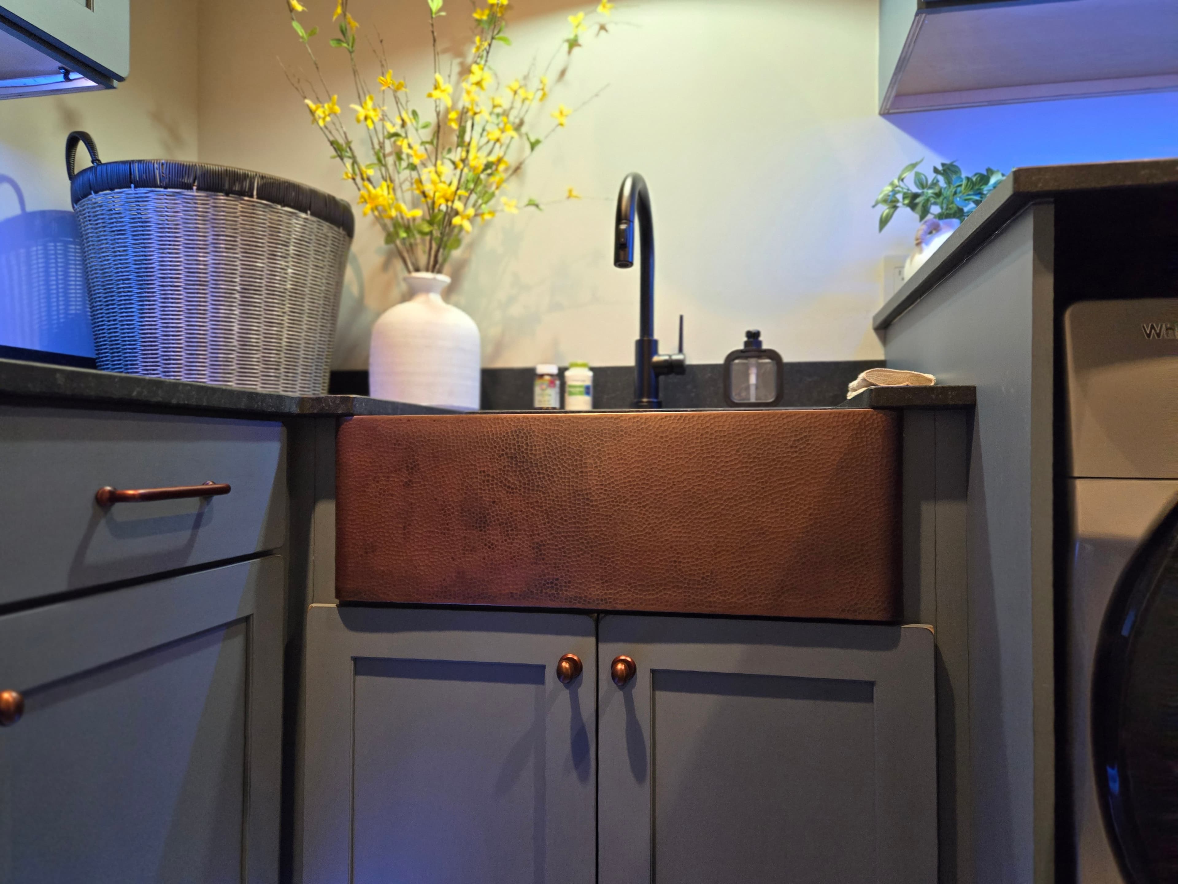 A laundry room with a copper farmhouse sink and fresh flowers